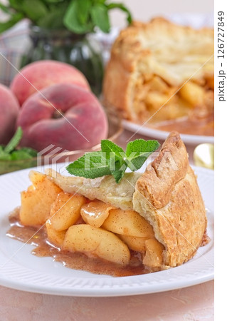 Delicious peach pie slice garnished with fresh mint, on white plate, vertical Delicious peach pie slice garnished with fresh mint, on white plate, vertical 126727849