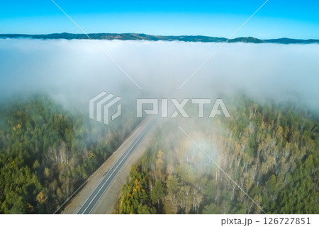 Aerial view of a winding road through green landscapes and fog-covered valleys under a clear blue sky 126727851