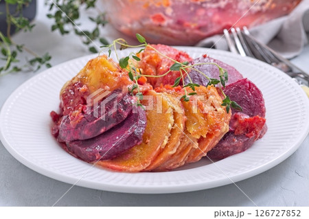 Sweet potato, parsnips and beet root gratin with thyme and melted cheese, on white plate, horizontal 126727852