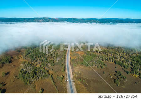 Aerial view of a winding road through green landscapes and fog-covered valleys under a clear blue sky Aerial view of a winding road through green landscapes and fog-covered valleys under a clear blue sky 126727854