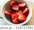 Sliced strawberries lie in a white plate against a wooden board and a white table. Macro photography of strawberries. Ripe red berries. Crops and fruits from the home garden 126727982