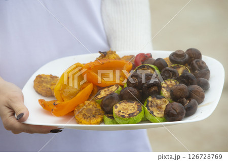 Hands hold a plate of grilled vegetables and mushrooms. Hands hold a plate of grilled vegetables and mushrooms. 126728769