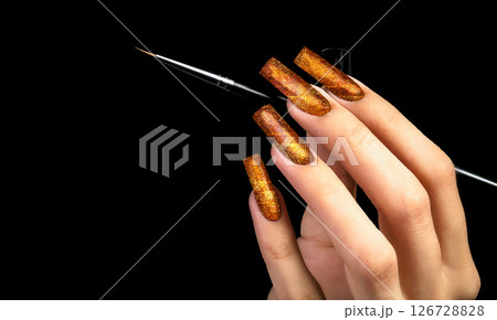 Hand with a beautiful gold manicure and a brush on a black background. Nail design. Extended nails. 126728828