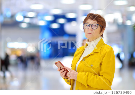 Portrait of elderly woman during shopping at mall. Red-haired senior lady using smartphone Portrait of elderly woman during shopping at mall. Red-haired senior lady using smartphone 126729490