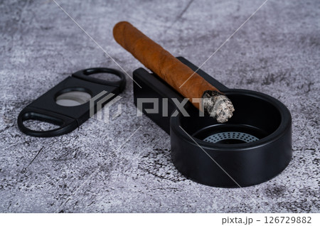 a lit cigar lies on an ashtray placed on the table 126729882