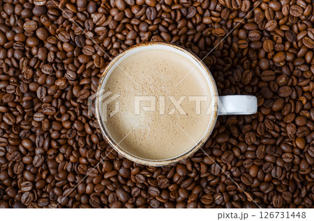 Coffee cup filled with creamy beverage surrounded by roasted coffee beans, showcasing rich textures and inviting aroma of freshly brewed coffee Coffee cup filled with creamy beverage surrounded by roasted coffee beans, showcasing rich textures and inviting aroma of freshly brewed coffee 126731448
