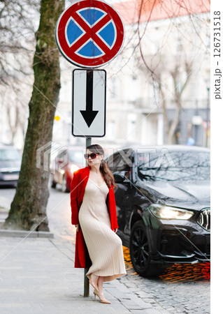 Stylish woman hailing a cab on a city street, wearing a red coat and sunglasses 126731518