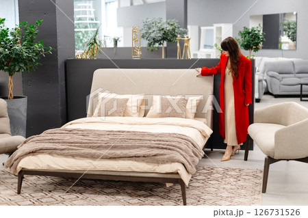 Woman choosing furniture in a showroom touching a beige double bed 126731526