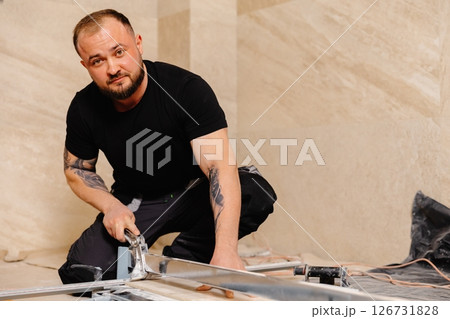 Construction worker cutting ceramic tile using manual tile cutter 126731828