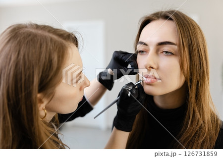 Young woman making makeup in a dressing makeup room. Lips make up process. Make-up artist in beauty studio doing makeup for beautiful girl Young woman making makeup in a dressing makeup room. Lips make up process. Make-up artist in beauty studio doing makeup for beautiful girl 126731859