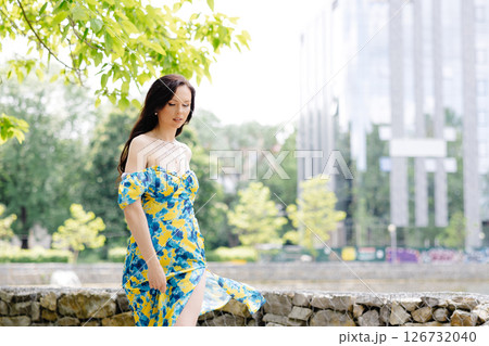 Young woman in summer dress is walking in green park and enjoying the sun. Playful and beautiful girl on warm sunny day. Young woman in summer dress is walking in green park and enjoying the sun. Playful and beautiful girl on warm sunny day. 126732040