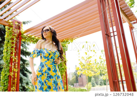 Beautiful young woman with long hair in trendy summer dress and sun glasses is walking in the park 126732048