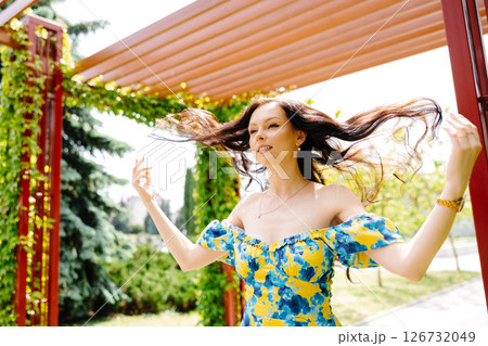 Young woman in summer dress is walking in green park and enjoying the sun. Playful and beautiful girl on warm sunny day. 126732049