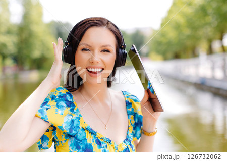 Attractive young woman with headphones listening to music via digital tablet a sunny day near lake Attractive young woman with headphones listening to music via digital tablet a sunny day near lake 126732062