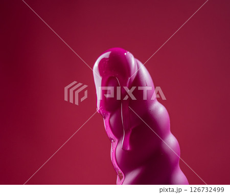Lube pouring on pink dildo on pink background.  126732499