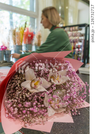 Close-up of a bouquet with white orchids and baby's breath flowers, with a florist working in the background. Floral business, holiday gifting 126732717