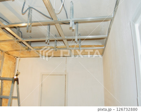 Installing ceiling metal frame with U-shaped brackets and mineral wool insulation for drywall - home renovation step Installing ceiling metal frame with U-shaped brackets and mineral wool insulation for drywall - home renovation step 126732880