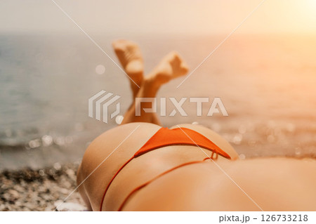 A woman sunbathes on the beach, lying on her stomach in a red swimsuit against the sea backdrop. 126733218