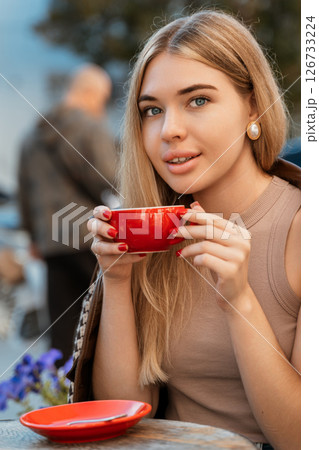 Woman Coffee Cafe - Young woman enjoying a cup of coffee while sitting at an outdoor cafe table. Woman Coffee Cafe - Young woman enjoying a cup of coffee while sitting at an outdoor cafe table. 126733224