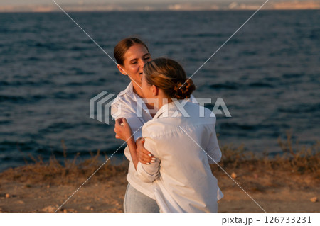 Couple Beach Sunset Hug - Two women embracing on the beach at sunset. Couple Beach Sunset Hug - Two women embracing on the beach at sunset. 126733231