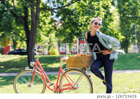 Portrait young adult pretty woman with red vintage retro bike and pin-up casual outfit green city park bright sunny summer day. Happy beautiful female person cycling outdoors. Healthy lifestyle 126733429