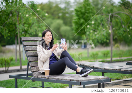 Woman making video call outdoors on lounge chair in park Woman making video call outdoors on lounge chair in park 126733931