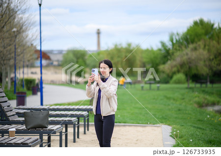 Woman making video call outdoors on lounge chair in park Woman making video call outdoors on lounge chair in park 126733935
