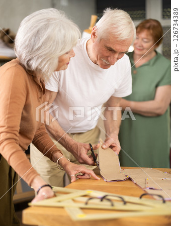 Elderly participants in sewing coterie learn sewing, communicate, cut pattern, work with mannequin Elderly participants in sewing coterie learn sewing, communicate, cut pattern, work with mannequin 126734389