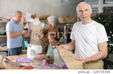 Elderly man showing paper pattern in training sewing workshop Elderly man showing paper pattern in training sewing workshop 126734398