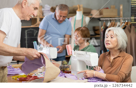 Elderly men and women sewing and discussing pattern in class Elderly men and women sewing and discussing pattern in class 126734442
