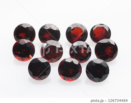 A stunning collection of round-cut, deep red natural garnets presented against a clean white background, showcasing their brilliance and clarity gemstones are arranged in an artful composition 126734484