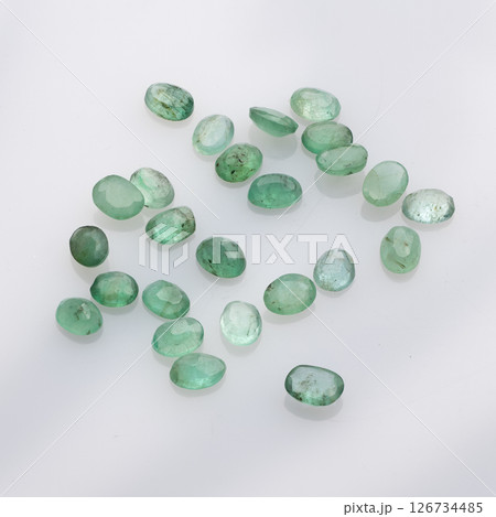 A captivating arrangement of loose, unpolished natural emerald gemstones in varying sizes and shades of green, scattered across a white background for visual appeal A captivating arrangement of loose, unpolished natural emerald gemstones in varying sizes and shades of green, scattered across a white background for visual appeal 126734485