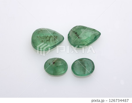Collection of four natural, uncut emerald gemstones in varying sizes and pear-like shapes displayed against a clean white background, exhibiting varying degrees of inclusions and vibrant green hues 126734487