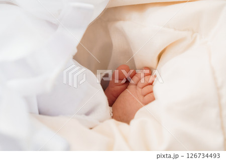 A close-up shot of a tiny baby's foot peeking out from under a soft, white blanket, evoking feelings of innocence, warmth, and new life 126734493