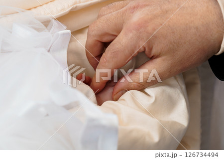A close-up shot of a man's hands delicately adjusting the layers of a luxurious, creamy white wedding dress, focusing on the meticulous detail and care involved in preparing for a wedding 126734494