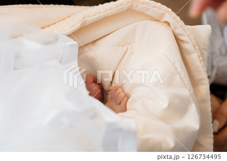 A close-up view of a newborn baby's tiny feet peeking out from under a soft, cream-colored blanket, representing the tenderness and vulnerability of new life 126734495