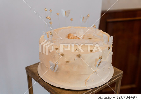 Beautifully Decorated Baby Shower Cake with a Sleeping Baby Topper and Golden Accents on a Wooden Stand, Featuring Stars and Butterflies Beautifully Decorated Baby Shower Cake with a Sleeping Baby Topper and Golden Accents on a Wooden Stand, Featuring Stars and Butterflies 126734497