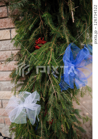 Festive Holiday Wreath Decoration with Evergreen Branches, Red Berries, and Blue and White Ribbons Against Brick Wall Background, Winter Season 126734522