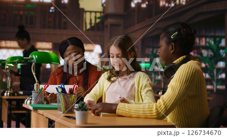 Preteens girls and their professor collaborating on schoolwork at the library, focused on academic materials to write a good essay. Students collect extra information with private lessons. Camera B. Preteens girls and their professor collaborating on schoolwork at the library, focused on academic materials to write a good essay. Students collect extra information with private lessons. Camera B. 126734670