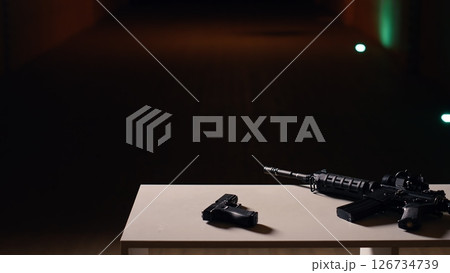 Practice weapons in military training outpost to be used by soldiers learning how to shoot firearms at paper target. Close up of pistol and rifle in army shooting range used for hitting bullseye 126734739