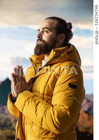 Pleased content hiker doing a meditation session for stress relief in nature, relaxing for wellness and balance on top of the mountain. Young hiker traveler meditating for mindfulness. Pleased content hiker doing a meditation session for stress relief in nature, relaxing for wellness and balance on top of the mountain. Young hiker traveler meditating for mindfulness. 126734746
