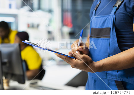 Technician investigating malfunctioning systems in photovoltaics factory, comparing parameters with pc and files. Black employee inspecting solar panels manufacturing plant, high tech. 126734775