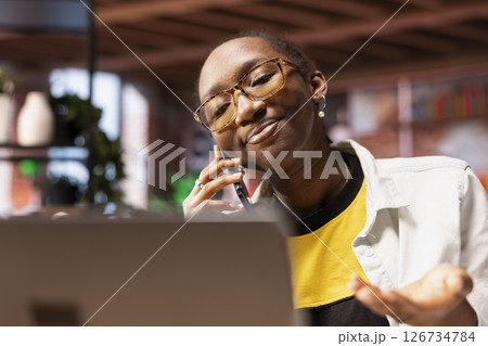 Upbeat woman having friendly conversation with friends during telephone call using smartphone. Happy african american person having fun catching up with mates, talking on phone Upbeat woman having friendly conversation with friends during telephone call using smartphone. Happy african american person having fun catching up with mates, talking on phone 126734784