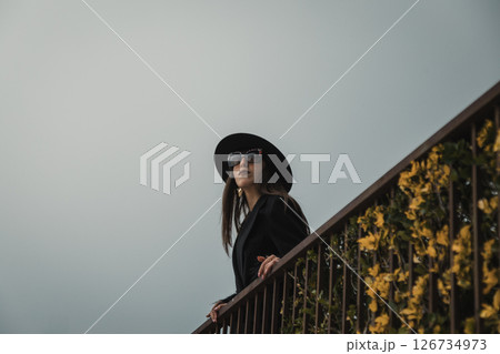 Elegant Coat Women Posing On The Railing In The Medieval Italian Town Square Elegant Coat Women Posing On The Railing In The Medieval Italian Town Square 126734973