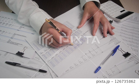 Focused Individual Completing Financial Paperwork and Calculations at a Desk in a Well-Lit Office Environment During Working Hours 126735862