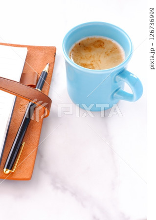 ミルクをたっぷり入れたコーヒー、カフェ・ラッテを飲みながら、システム手帳でデスクワーク中のイメージ 126736999