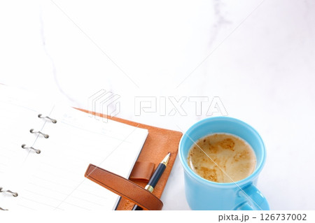 ミルクをたっぷり入れたコーヒー、カフェ・ラッテを飲みながら、システム手帳でデスクワーク中のイメージ ミルクをたっぷり入れたコーヒー、カフェ・ラッテを飲みながら、システム手帳でデスクワーク中のイメージ 126737002
