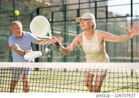 Motivated senior man and woman playing padel with his teammate in court 126737637
