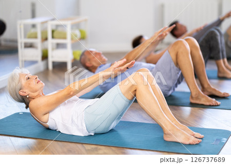 Group of elderly women and men practicing pilates exercises in gym. Abdominal press training Group of elderly women and men practicing pilates exercises in gym. Abdominal press training 126737689