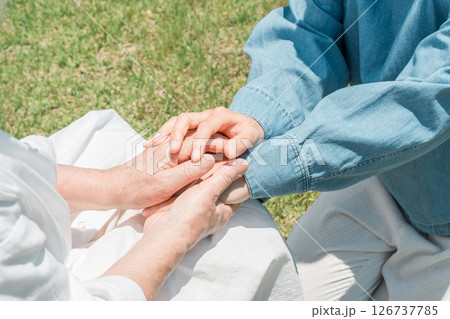 車椅子に座るシニア女性の手を握る孫娘の手元 126737785
